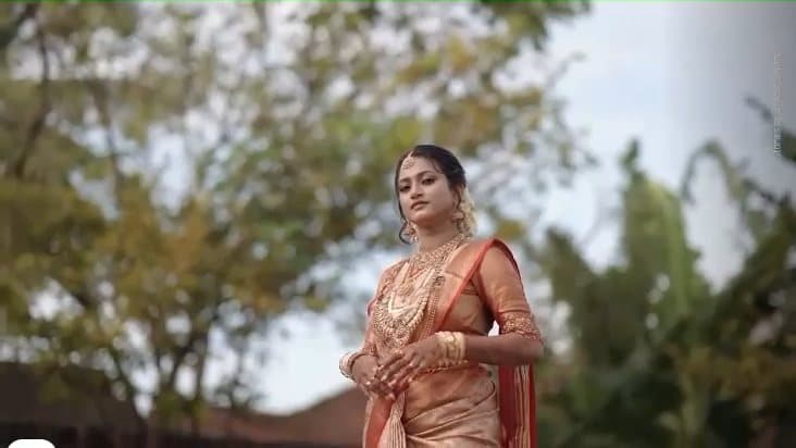 A bride in a gold silk saree and traditional jewellery, outdoors.