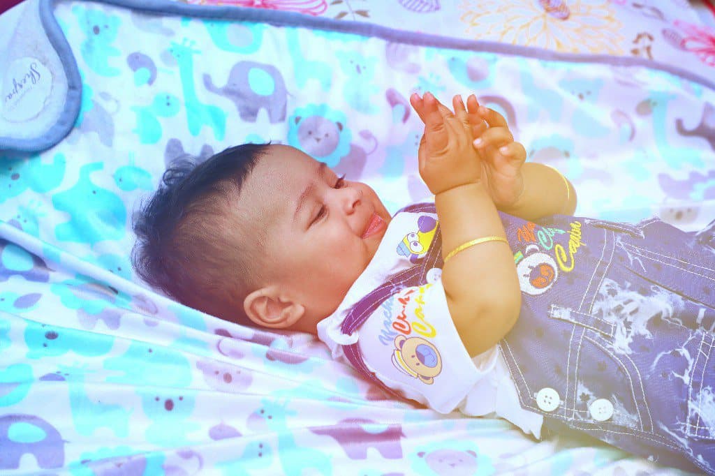 A baby lying on a patterned blanket, playing with their hands.